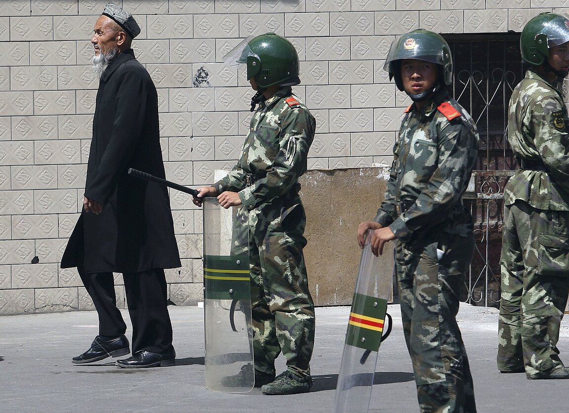 An Uighur man and Chinese officers in Xinjiang An Uighur man and Chinese officers in Xinjiang