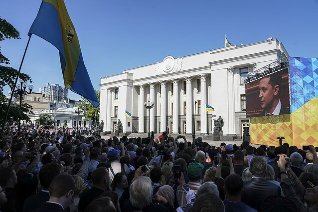 People gather in front of Verkhovna Rada, the Ukrainian parliament, during the inauguration ceremony of new Ukrainian President Volodymyr Zelenskiy, right on the screen, in Kiev, Ukraine, Monday, May 20, 2019. 