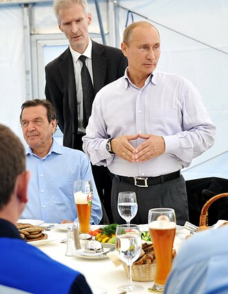 Russian Prime Minister Vladimir Putin, standing right, and former German Chancellor Gerhard Schröder, seated left, in 2011