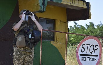 A Ukrainian soldier looks through binoculars at a checkpoint in Mayorsk, Donetsk region