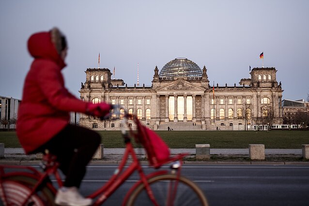 A woman rides past the Reichstag building, the seat of the German Bundestag in Berlin.