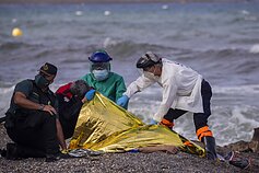 Medikai apžiūri kūną migranto, kuris mirė galimai bandydamas apiplaukti Ispanijos anklavo sieną 2021-ųjų gegužės mėnesį.
