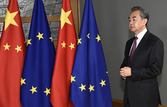 Kinijos užsienio reikalų ministras Wangas Yi stovi prie Kinijos ir Europos Sąjungos vėliavų
