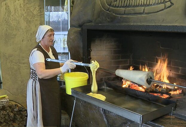 Kepėja M. Gudonienė į įkaitusią skarda pila šakočio tešlą Kepėja M. Gudonienė į įkaitusią skarda pila šakočio tešlą