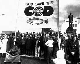 Islandijos demonstrantai laiko užrašą „Dieve, saugok menkes“. 1973 m. gegužės 24 d., ketvirtadienį, Reikjavike vykusiame protesto mitinge prieš Didžiosios Britanijos karinio jūrų laivyno įplaukimą į ginčijamus 50 jūrmylių Islandijos žvejybos vandenis.