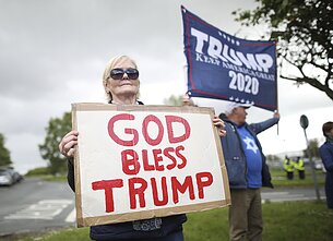 Moteris laiko plakatą su užrašu „Dieve, laimink Trumpą“