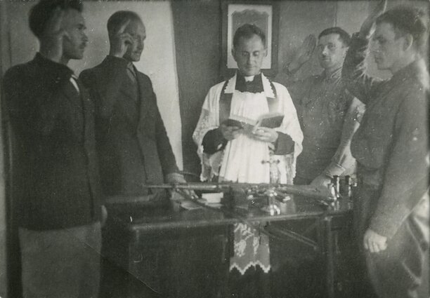 Pirmojo Tauro apygardos štabo pareigūnų priesaika. Skardupių klebonija (Marijampolės vlsč.), 1945 m. liepos 19 d. Iš kairės stovi: Jonas Pileckis-Brokas, apygardos vadas Leonas Taunys-Kovas, apygardos kapelionas Antanas Ylius-Vilkas, Albinas Ratkelis-Oželis ir Vytauto rinktinės vadas Vytautas (Vitalius) Gavėnas-Vampyras Pirmojo Tauro apygardos štabo pareigūnų priesaika. Skardupių klebonija (Marijampolės vlsč.), 1945 m. liepos 19 d. Iš kairės stovi: Jonas Pileckis-Brokas, apygardos vadas Leonas Taunys-Kovas, apygardos kapelionas Antanas Ylius-Vilkas, Albinas Ratkelis-Oželis ir Vytauto rinktinės vadas Vytautas (Vitalius) Gavėnas-Vampyras