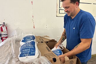 Savanoris iš „Kanbe's Markets“ nevyriausybinės organizacijos, tiekiančios šviežias ir prieinamas maisto prekes nepasiturinčioms bendruomenėms Kanzaso mieste, apžiūri dėžę šaldytų kalakutų