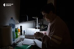 Nina in her apartment in Kyiv during a power and heating outage. The woman is retired and has been helping her son Taras care for her grandson Bohdan, an adult man with severe cerebral palsy, for over a year.