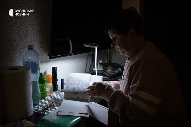 Nina in her apartment in Kyiv during a power and heating outage. The woman is retired and has been helping her son Taras care for her grandson Bohdan, an adult man with severe cerebral palsy, for over a year.