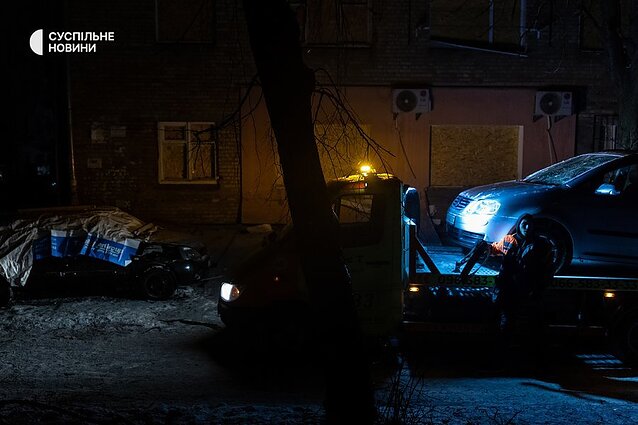A tow truck takes away cars parked near the house that have been smashed by drone debris.