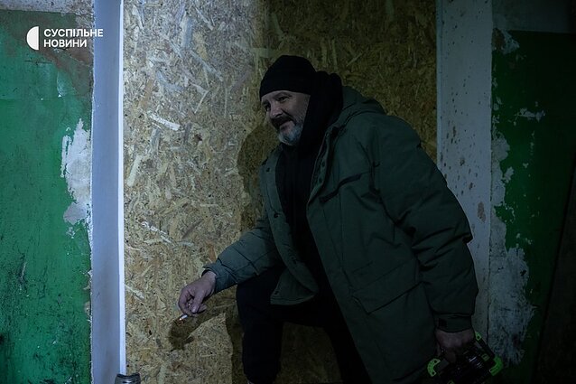 Serhii, a resident of a high-rise building, shows plywood where yesterday there was a window.