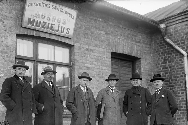 Šiaulių kraštotyros draugijos valdybos nariai prie pirmojo „Aušros“ muziejaus pastato. Apie 1927 m. Iš kairės stovi: Šiaulių miesto burmistras Jackus Sondeckis, Šiaulių „Aušros“ muziejaus bei vienas iš kraštotyros draugijos steigėjų Peliksas Bugailiškis, kraštotyrininkas, gydytojas Domas Jasaitis, Šiaulių kraštotyros draugijos vicepirmininkas Balys Petrauskas, Šiaulių Šv. Petro ir Povilo bažnyčios klebonas Stanislovas Sarapas, Šiaulių apskrities valdybos pirmininkas Julijonas Švambaris