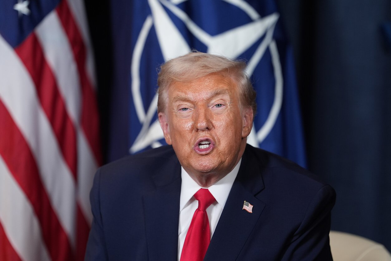 Donaldas Trumpas priešais NATO ir JAV vėliavas