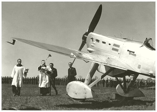 1937 m. Kauno aerodrome krikštijami naujieji naikintuvai „Dewoitine D-501L“. Kapelioną lydi Leonardas Peseckas ir Jonas Mikėnas 1937 m. Kauno aerodrome krikštijami naujieji naikintuvai „Dewoitine D-501L“. Kapelioną lydi Leonardas Peseckas ir Jonas Mikėnas