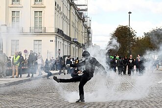 Protestuotojas spiria ašarinių dujų kapsulę